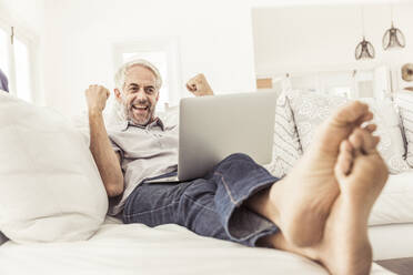 Älterer Mann mit Laptop, der zu Hause auf der Couch jubelt - SDAHF00330