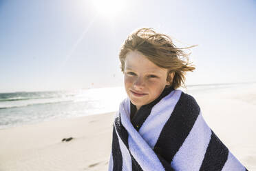 Portrait of smiling boy wrapped in a towel on the beach - SDAHF00344