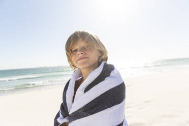 Porträt eines lächelnden Jungen, eingewickelt in ein Handtuch, am Strand - SDAHF00345