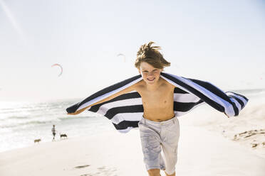 Porträt eines Jungen, der mit einem Handtuch am Strand läuft - SDAHF00346