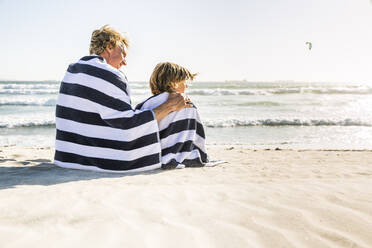 Vater mit Sohn, eingewickelt in ein Handtuch, am Strand - SDAHF00348