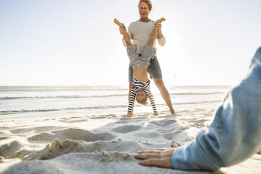 Vater hilft Sohn bei einem Handstand am Strand - SDAHF00353