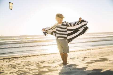 Junge mit einem Handtuch am Strand bei Sonnenuntergang, lizenzfreies Stockfoto