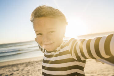 Porträt eines lächelnden Jungen mit einem Handtuch am Strand bei Sonnenuntergang - SDAHF00364