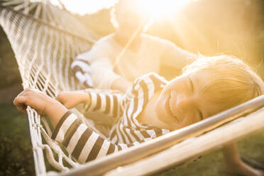 Portrait of smiling boy lying in hammock with father in background - SDAHF00367