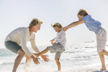 Father having fun with his sons on the beach, running and jumping in the sand - SDAHF00379