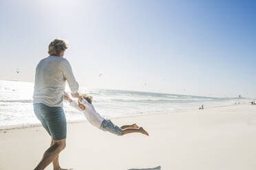 Ein Vater hat Spaß mit seinem Sohn am Strand und wirbelt ihn herum - SDAHF00382