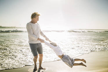 Ein Vater hat Spaß mit seinem Sohn am Strand und wirbelt ihn herum - SDAHF00395