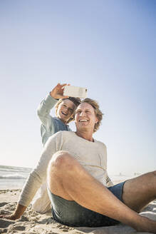 Father having fun with his son on the beach, taking smartphone pictures - SDAHF00396