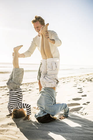 Vater hat Spaß mit seinem Sohn am Strand und übt Kopfstand, lizenzfreies Stockfoto