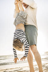 Father having fun with his son on the beach, holding him upside down - SDAHF00401