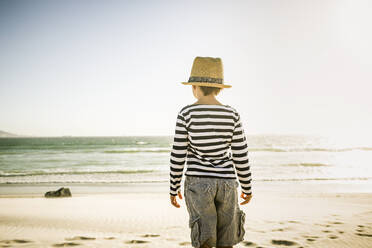 Rear view of boy with hat standing on the beach - SDAHF00418