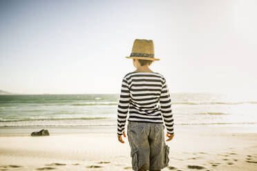 Rückansicht eines am Strand stehenden Jungen mit Hut - SDAHF00418