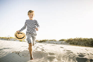 Fröhlicher Junge mit Hut läuft am Strand - SDAHF00419