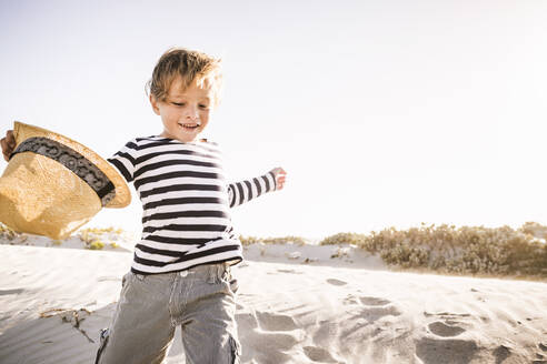 Fröhlicher Junge mit Hut läuft am Strand - SDAHF00420