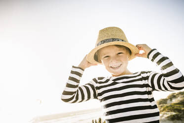 Porträt eines glücklichen Jungen mit Hut am Strand - SDAHF00424