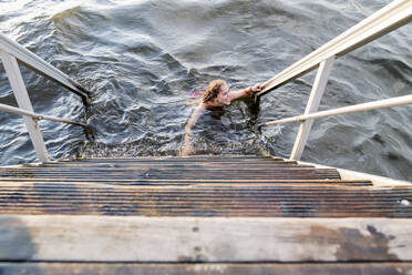 Woman swimming in lake next to wooden steps - JOHF08287