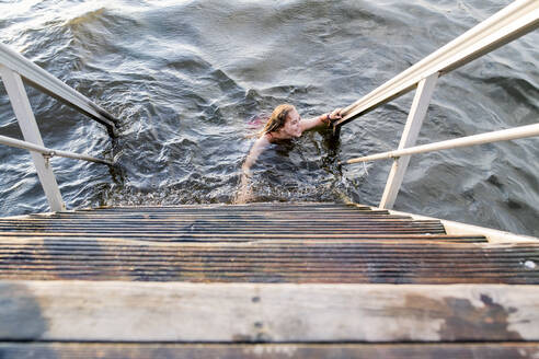 Frau schwimmt im See neben einer Holztreppe - JOHF08287