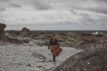 Junge Frau geht an felsiger Küste spazieren - JOHF08417