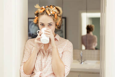 Portrait of young woman with curlers in hair drinking coffee - SDAHF00435