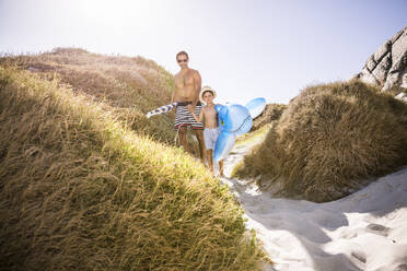 Vater und Sohn mit aufblasbarem Hai wandern durch die Dünen zum Strand - SDAHF00445