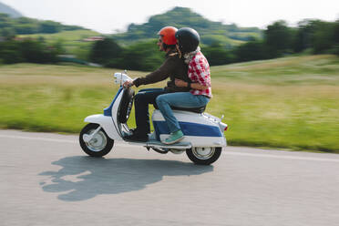 Couple riding vintage motor scooter on country road, Tuscany, Italy - GIOF07987