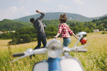 Happy couple with vintage motor scooter jumping on a meadow, Tuscany, Italy - GIOF07990