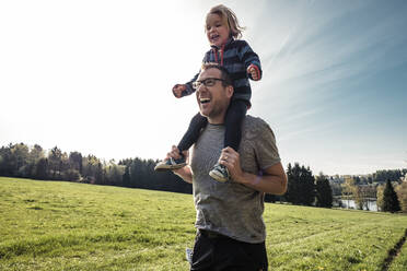 Porträt eines lachenden Vaters, der seine kleine Tochter auf den Schultern trägt, auf einer Wiese - WFF00268