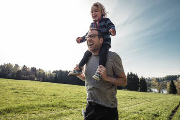 Portrait of laughing father carrying little daughter on his shoulders on a meadow - WFF00268