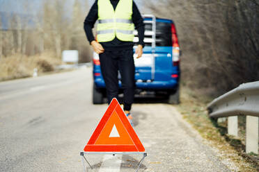Man putting warning triangle on country road by van breakdown - CJMF00255