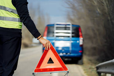 Man putting warning triangle on country road by van breakdown - CJMF00256