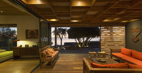Illuminated modern, luxury home showcase interior living room open to patio - HOXF04908