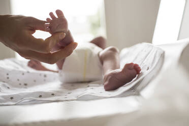Mother holding tiny foot of newborn baby son laying on changing table - HOXF04918