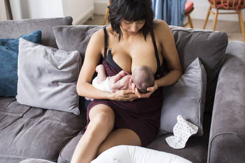 Mutter, die ihr neugeborenes Kind auf dem Sofa stillt - HOXF04923