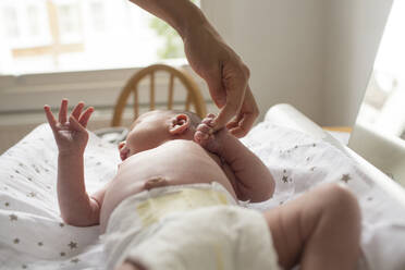 Mother holding hands with newborn baby son laying on changing table - HOXF04927