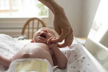 Mother holding hands with crying newborn baby son on changing table - HOXF04929