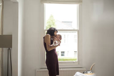 Mutter küsst neugeborenen Sohn im Fenster - HOXF04937