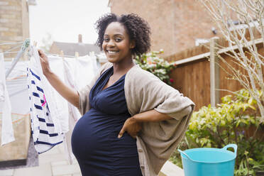 Porträt schöne schwangere Frau hängt Kleidung auf Wäscheleine - HOXF04942