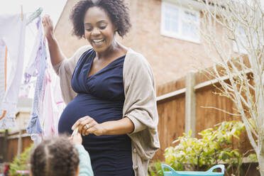 Happy pregnant woman hanging clothes on clothesline - HOXF04944