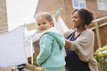 Portrait happy girl helping pregnant mother hang laundry on clothesline - HOXF04945