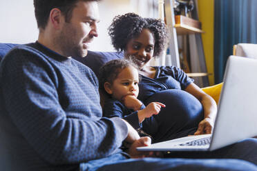 Junge schwangere Familie mit Laptop auf dem Sofa - HOXF04946