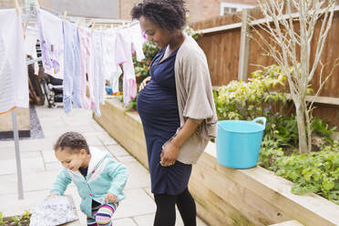 Pregnant mother and daughter hanging laundry on clothesline - HOXF04952