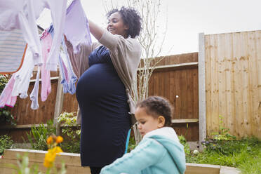 Pregnant woman with daughter hanging laundry on clothesline - HOXF04953