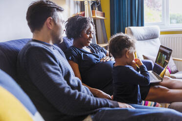 Schwangere Familie mit Laptop auf dem Sofa - HOXF04962