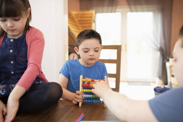 Junge mit Down-Syndrom und Geschwister spielen mit Spielzeug am Tisch - HOXF04981