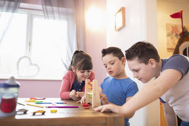 Junge mit Down-Syndrom und Geschwister spielen mit Spielzeug am Tisch - HOXF04985