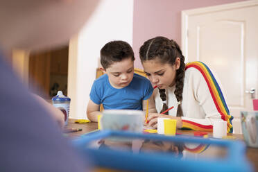 Boy with Down Syndrome and sister coloring at table - HOXF04988