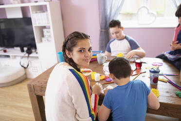 Portrait smiling teenage girl playing with siblings at table - HOXF04990