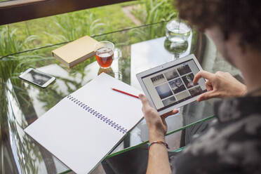 Young man looking at photographs on digital tablet in home office - HOXF04999