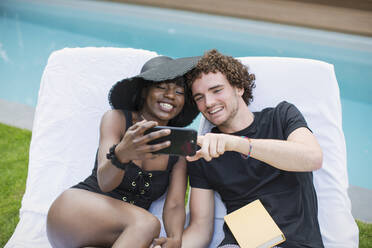 Happy young couple taking selfie with camera phone at poolside - HOXF05006